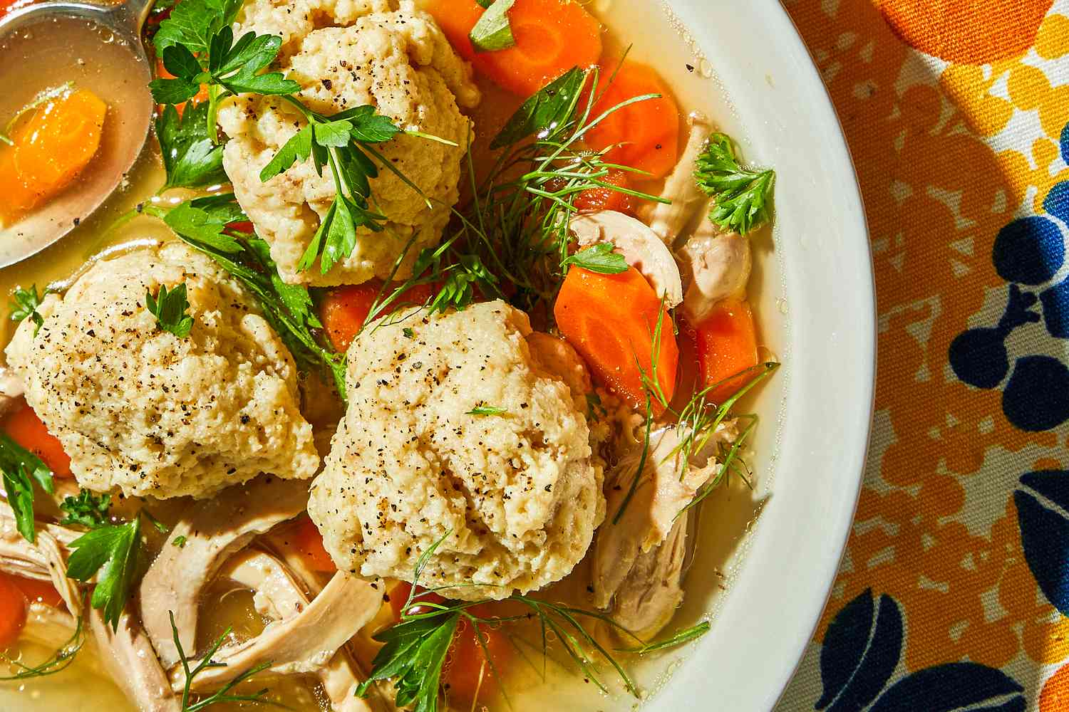 Matzo ball soup in a white bowl on a flowered tablecloth
