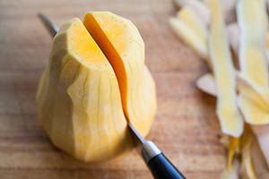 A knife cutting a peeled butternut squash in half