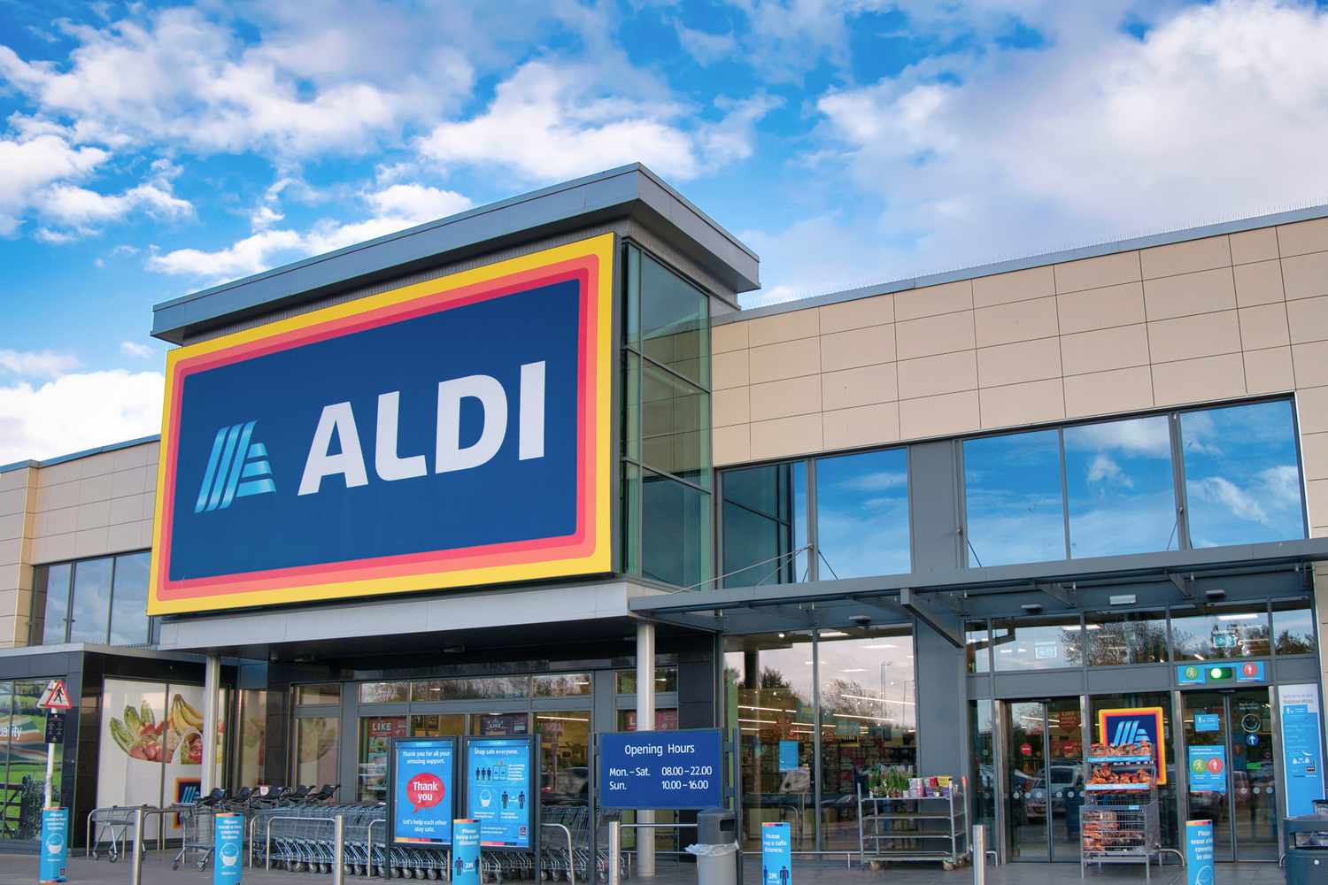 The exterior entrance of an Aldi supermarket with signage and glass windows, located under a bright sky