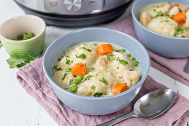 A blue bowl on a pink cloth filled with chicken and dumplings with an instant pot in the background.
