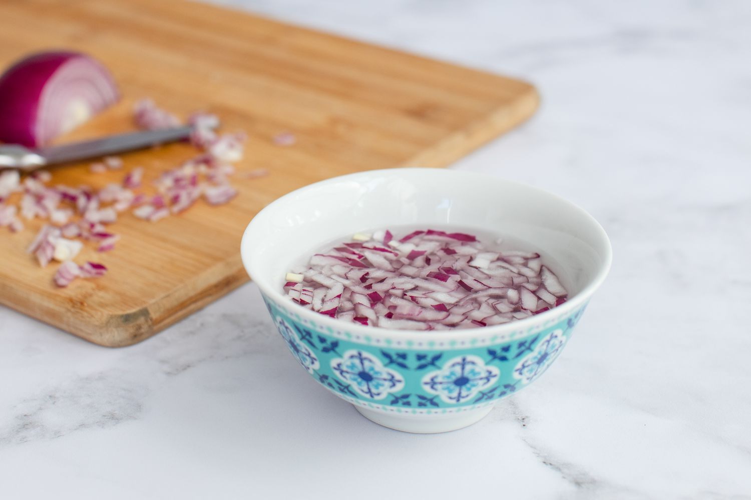 Chopped red onion in a bowl of liquid to make a green bean salad recipe.