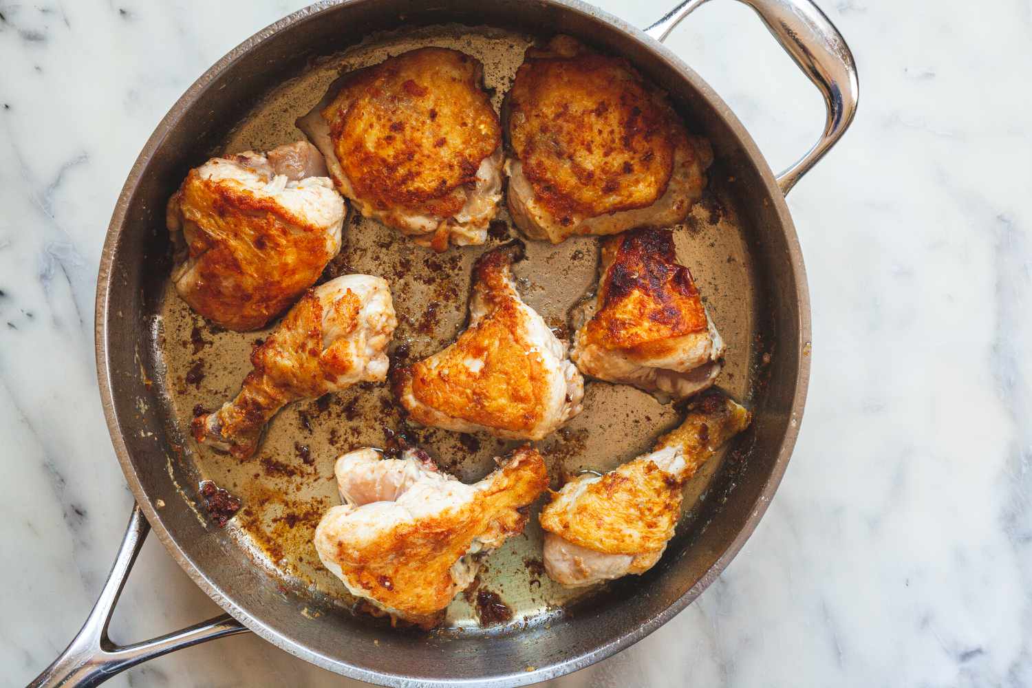 Overhead view of browning chicken pieces in a skillet.