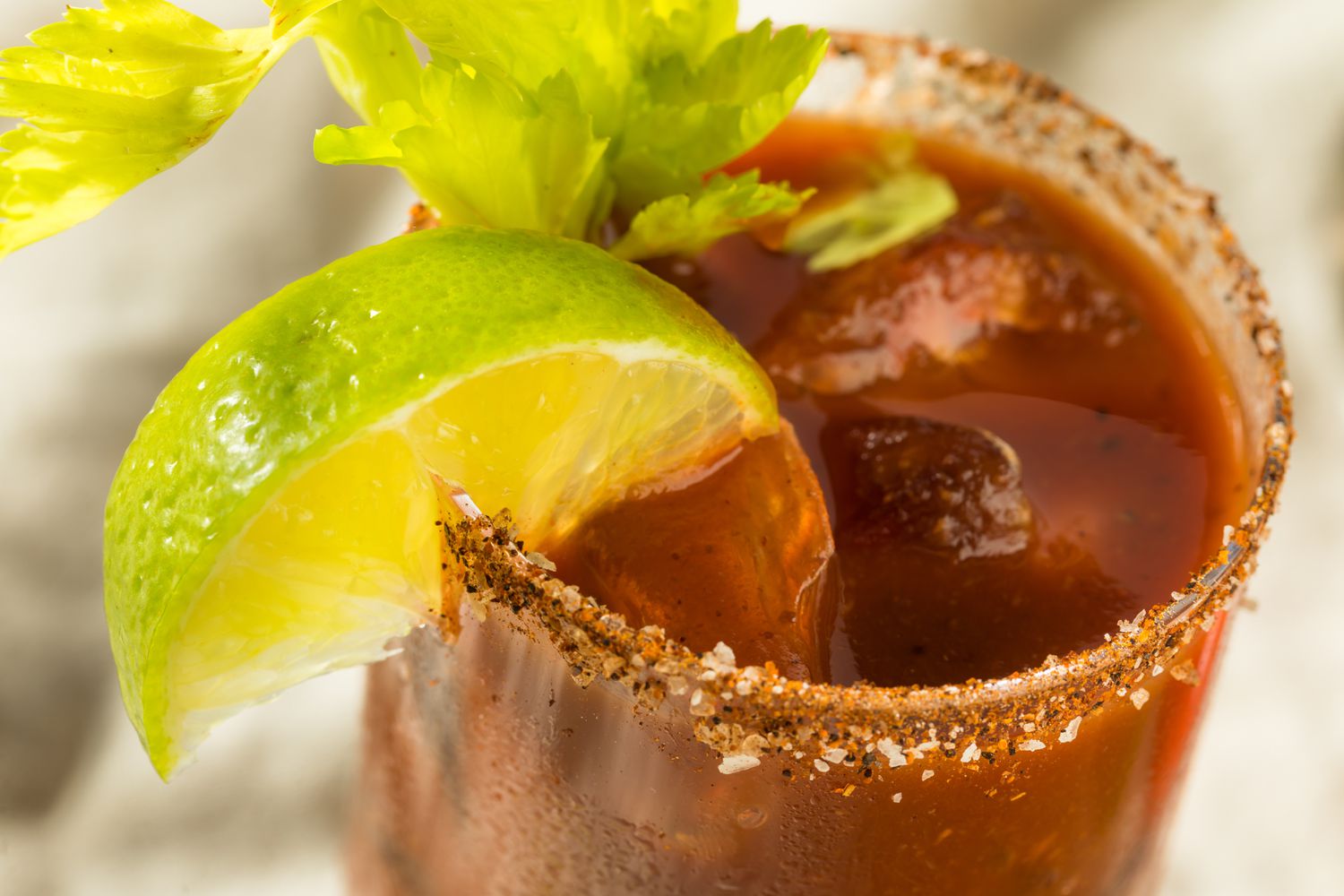 A closeup of a salt-rimmed glass with bloody Mary, garnished with a lime wedge and lime wedge
