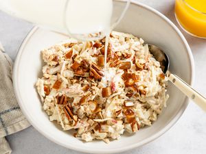 Overhead shot of a bowl of muesli with a spoon, and milk getting poured in from a glass