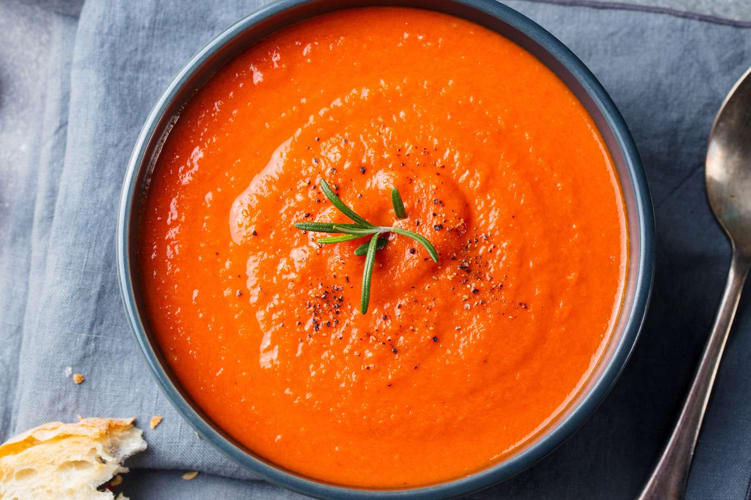 A bowl of tomato soup garnished with a sprig of rosemary