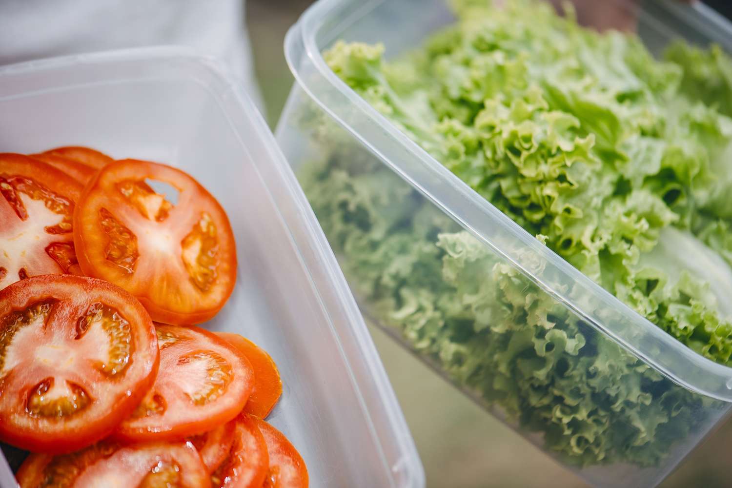 Containers of sliced tomatoes and leafy lettuce used for food preparation or storage