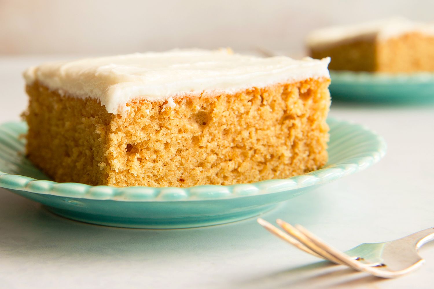 A slice of cake with icing on a plate with a fork nearby