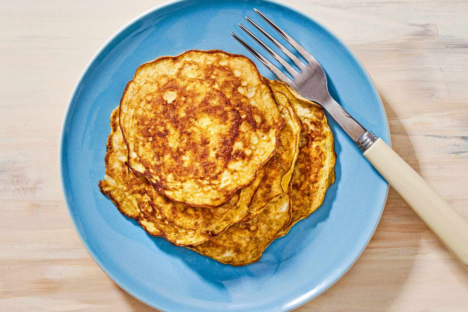 Overhead view of a blue plate of 2-ingredient pancakes with a fork on a wooden tabletop