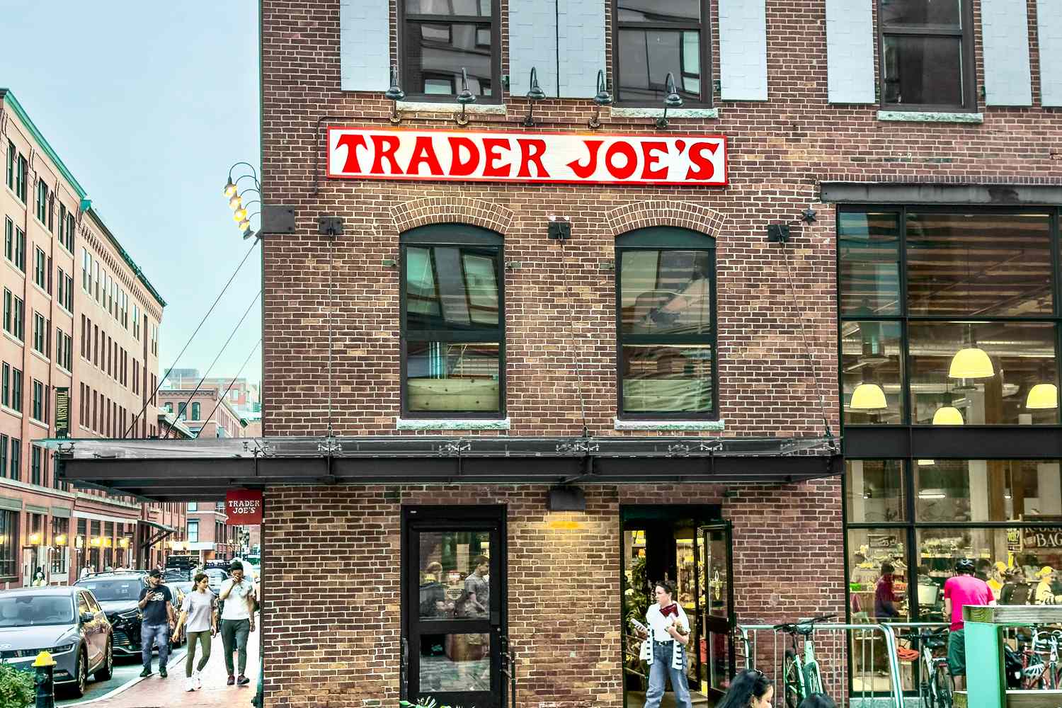 A brick building with a Trader Joes store people walking on a street outside