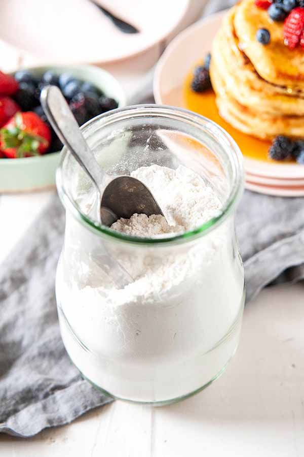Pancake mix in glass jar with pancakes in the background