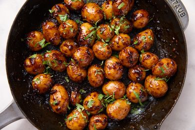 A skillet filled with sticky roasted potatoes garnished with herbs