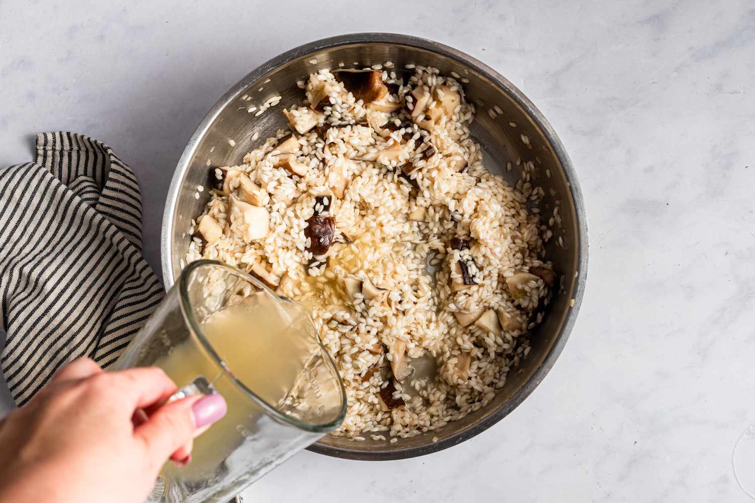 A stock being poured into the risotto dish 