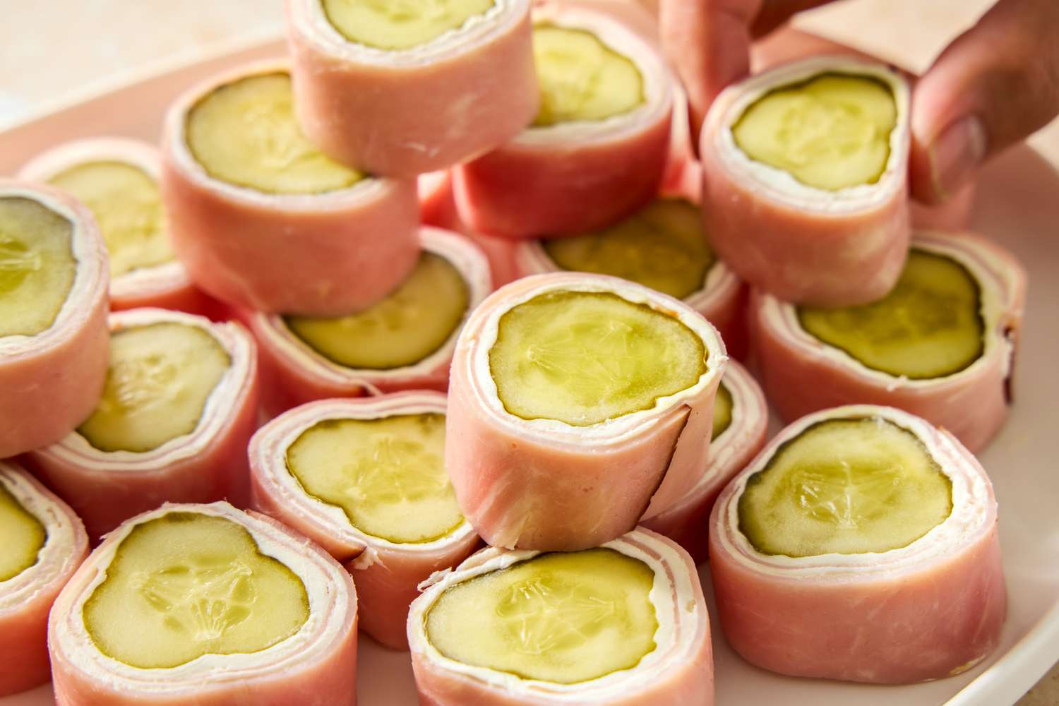Pickle and cream cheese rollups wrapped in ham arranged on a platter
