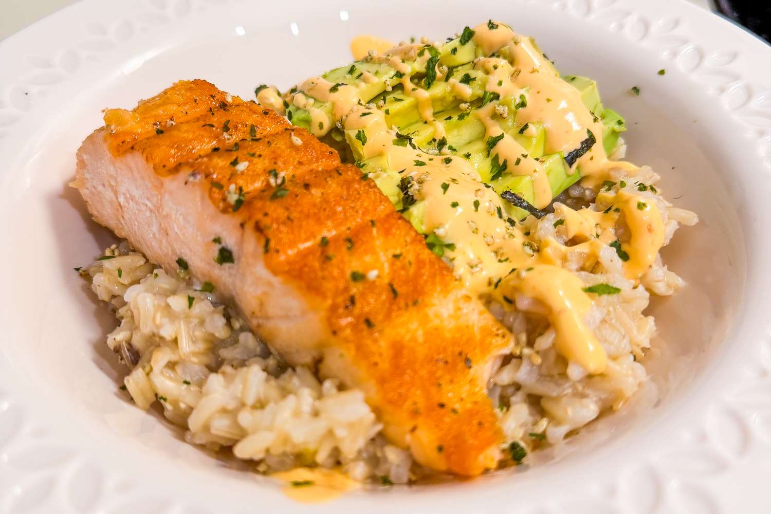 Seared salmon on rice with avocado and sauce garnished with herbs