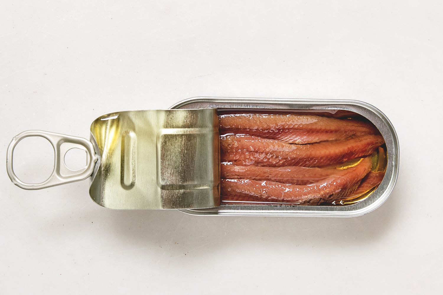 Canned sardines with an open pull-tab lid, showing the fillets inside