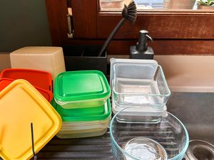 Plastic and glass food storage containers drying on a dish rack near a sink