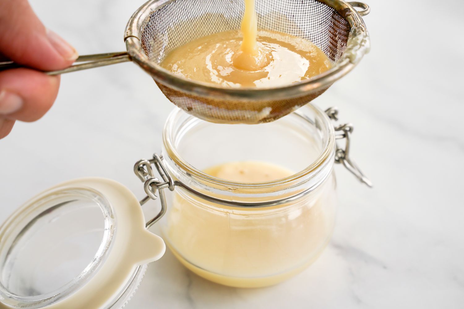 Homemade Condensed Milk Run Through a Sieve Into a Jar 
