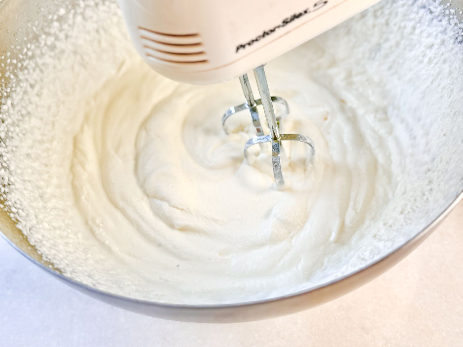 An electric hand mixer blending cream in a mixing bowl