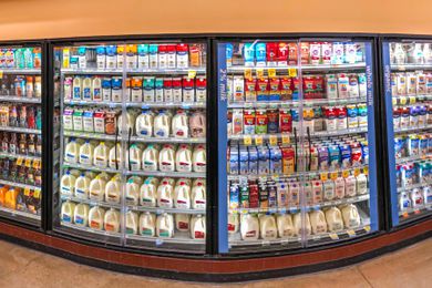 Dairy products displayed in refrigerated sections at a store, including various milk brands in cartons and jugs