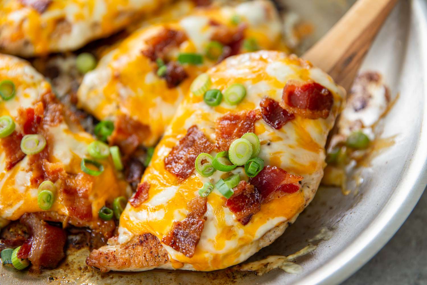 Dish of cooked chicken breasts topped with melted cheese, bacon, and green onions