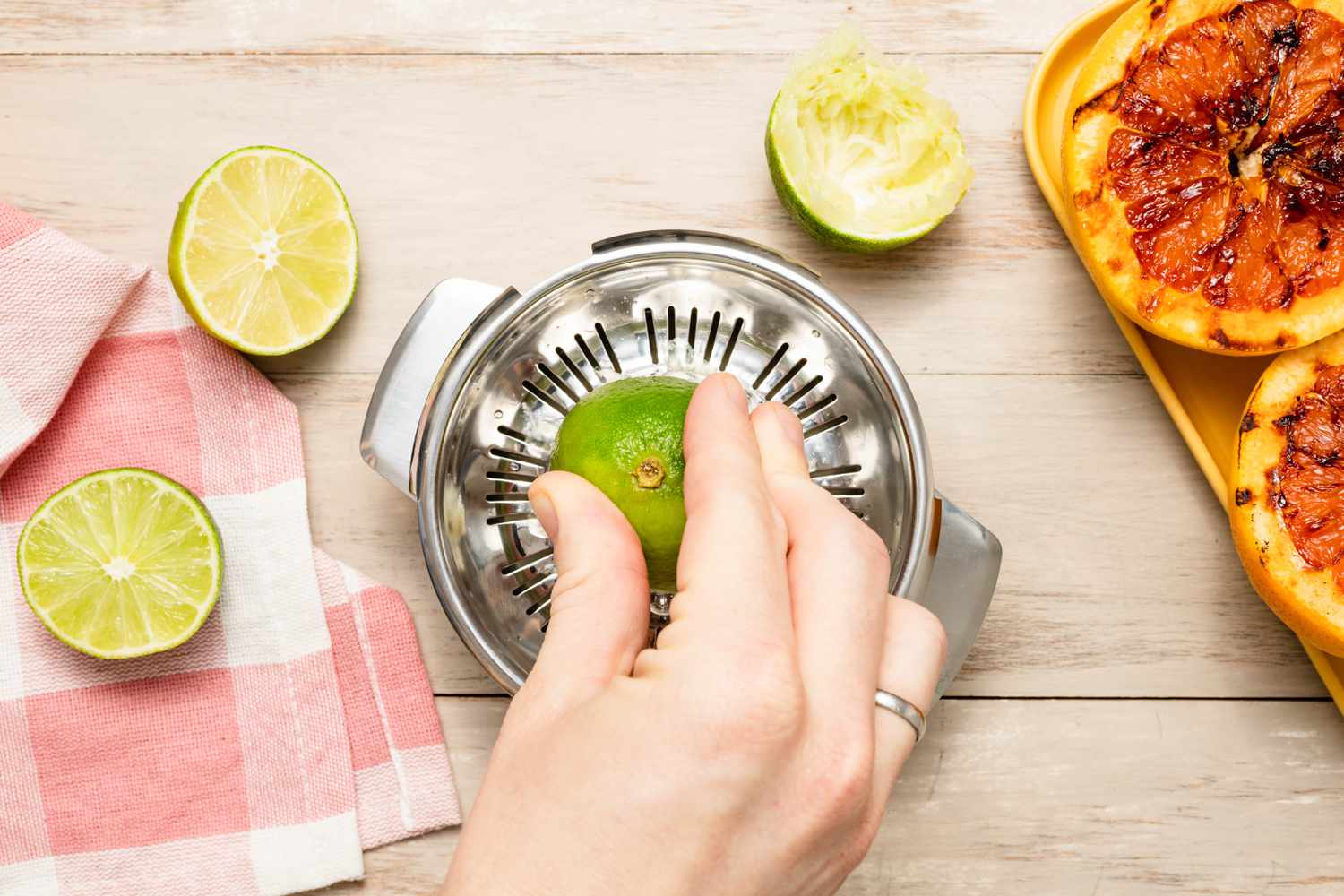 Halved Lime Pressed Into a Tabletop Citrus Juicer, and in the Surroundings, More Halved Limes With One Already Juiced and a Tray of Grilled Grapefruit 