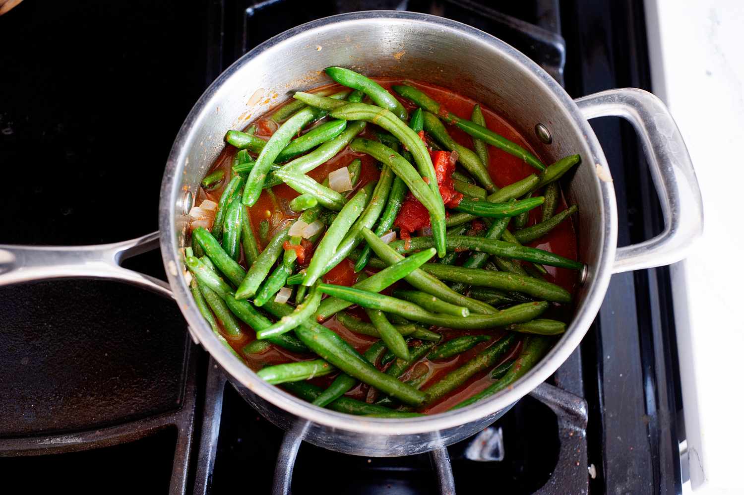Green beans added to a pot of onions and tomatoes on the stove to make Turkish green beans.