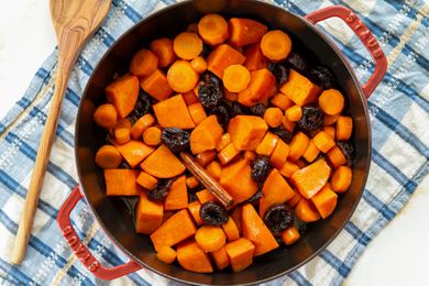 overhead view of Carrot and Sweet Potato Tzimmes in a roasting pan with a wooden spoon