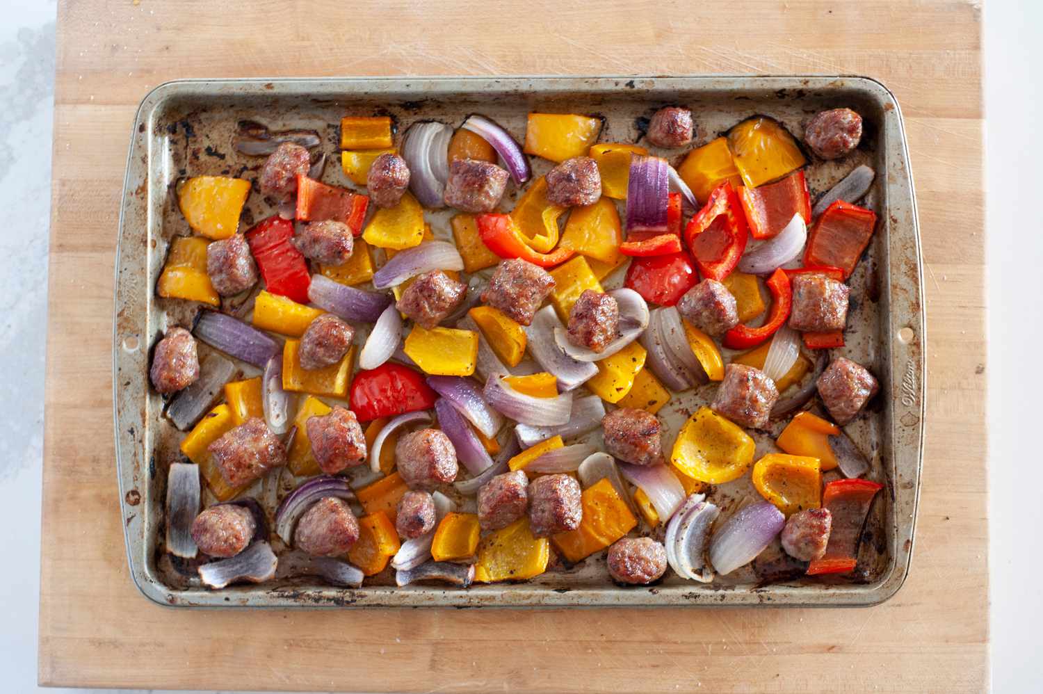 Sheet pan sausage dinner on a wooden block.
