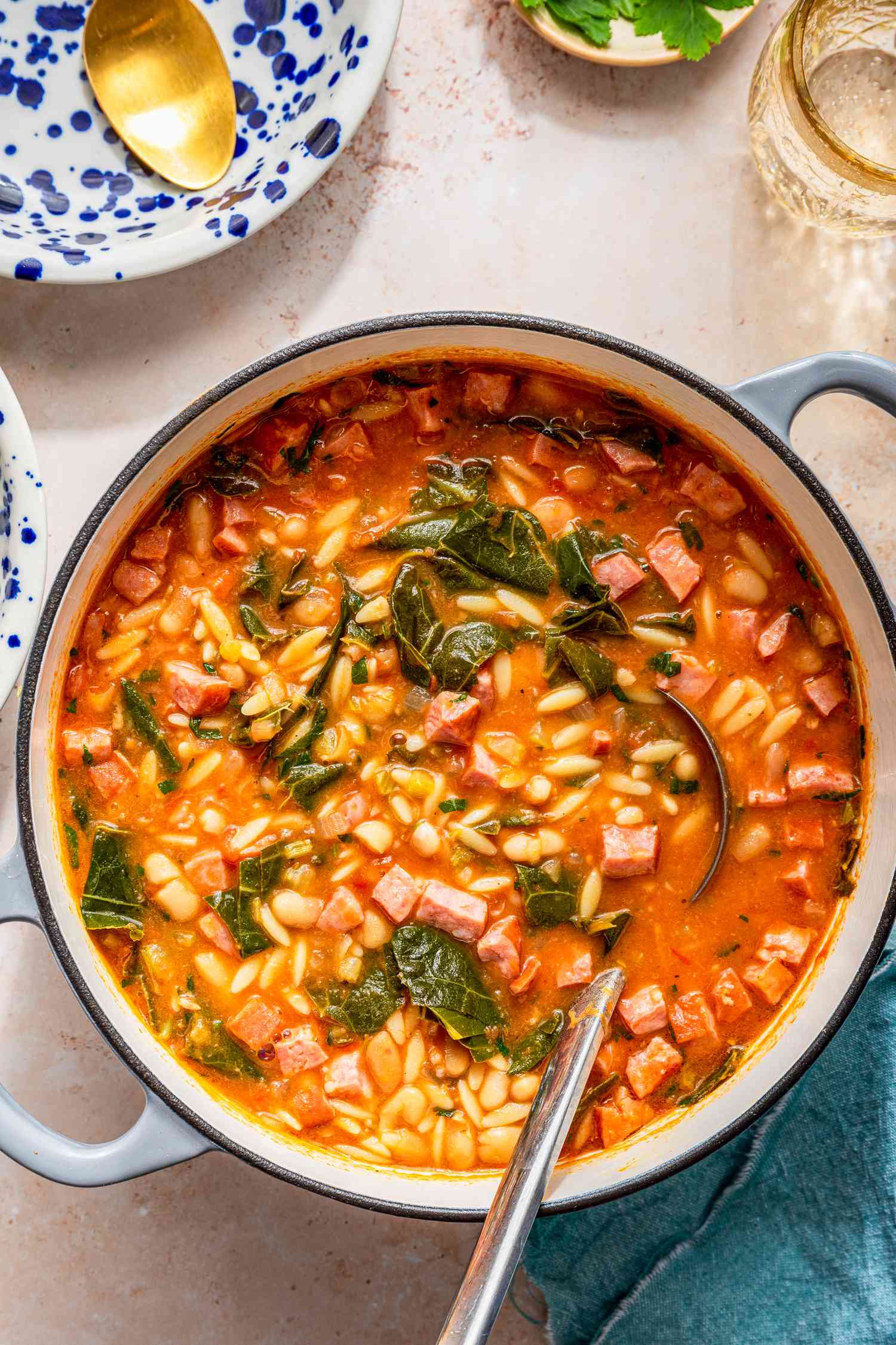 Swamp soup in a dutch oven at a table setting with a bowl of parsley, a glass of water, a bowl of crackers, and a spoon