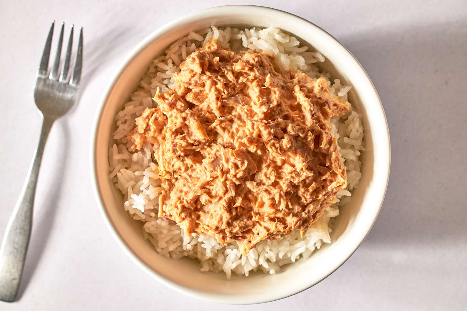 Bowl of rice topped with shredded spicy tuna, fork placed to the side.