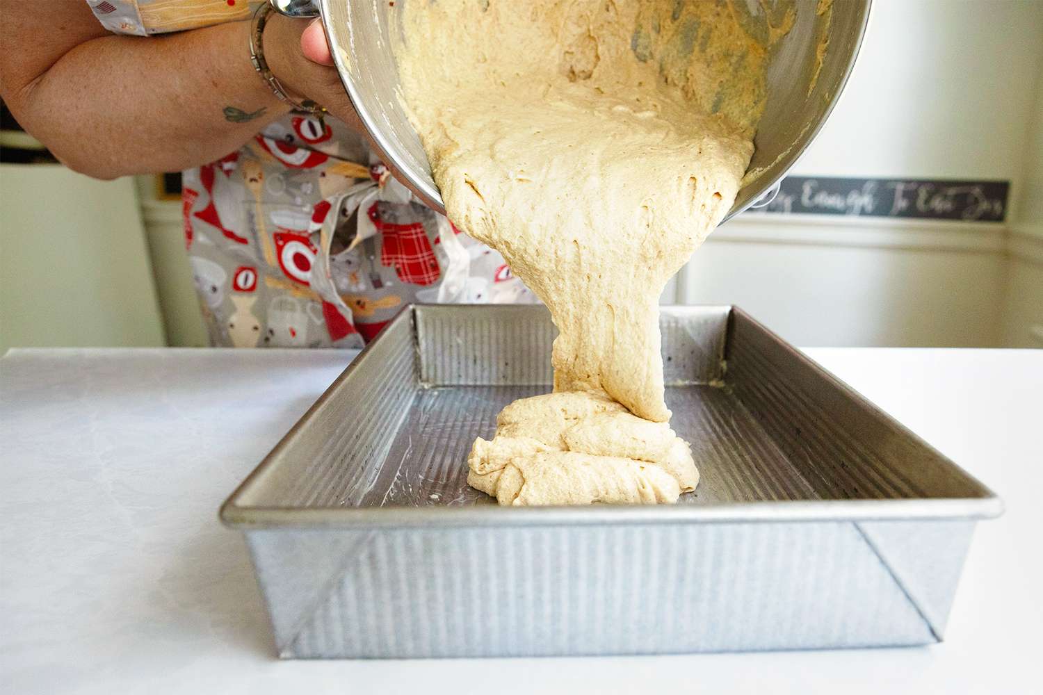 Person pouring cake batter into a rectangular baking tin