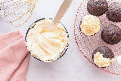 Creamy French buttercream frosting in a bowl with chocolate cupcakes to the right of it.