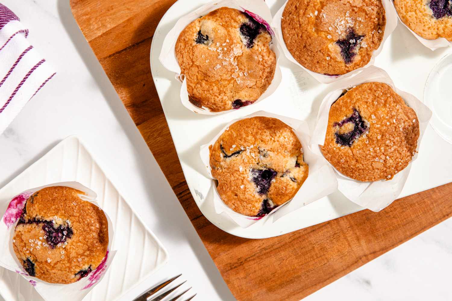 Blueberry muffins in a tray and one on a plate with a fork nearby