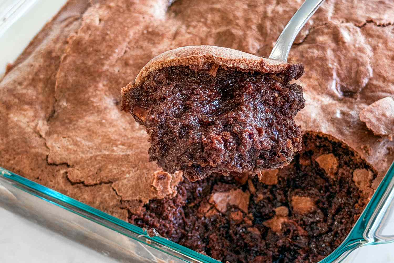 A serving of brownie pudding being scooped from a baking dish