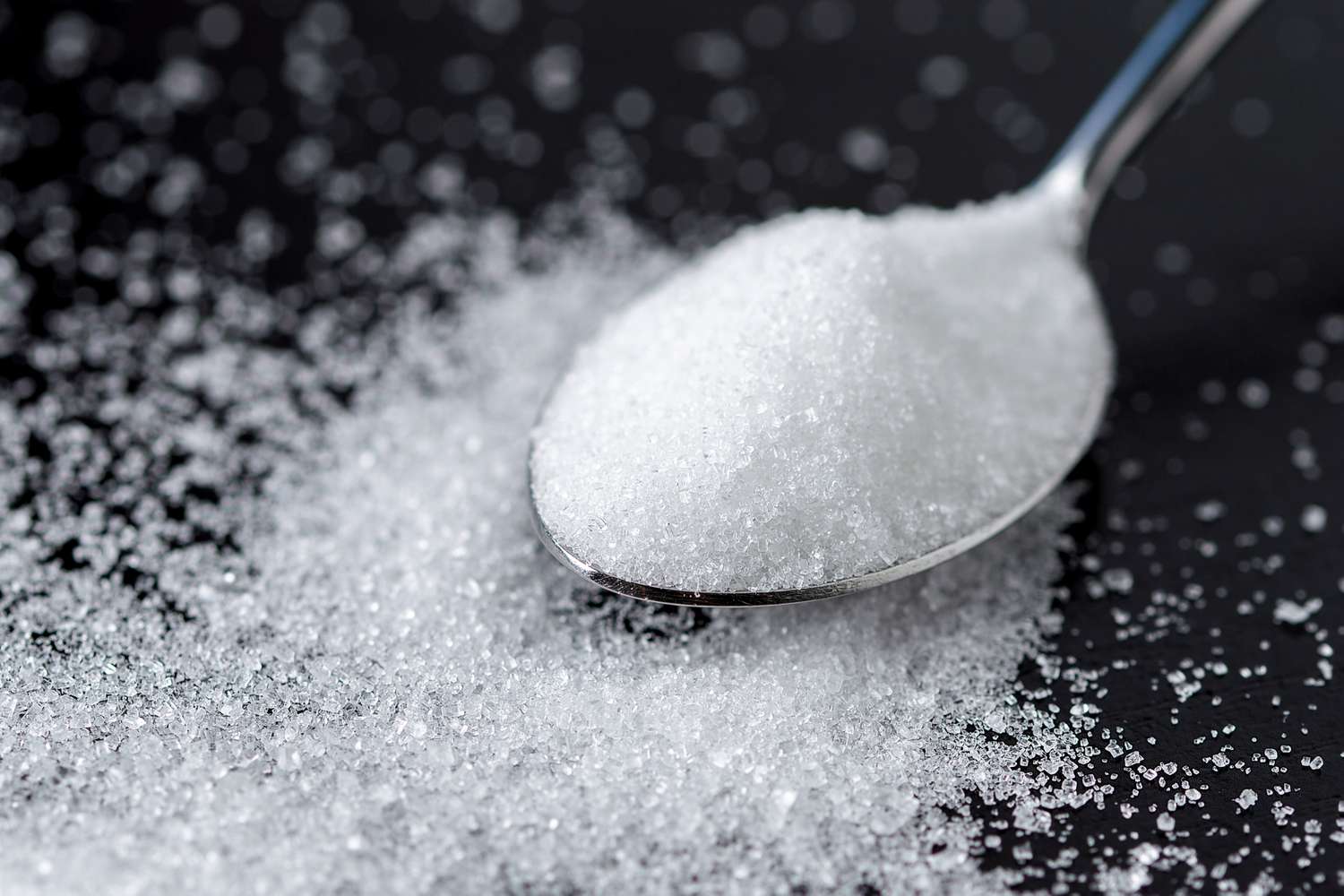 A closeup of a spoon with granulated sugar sugar scattered around