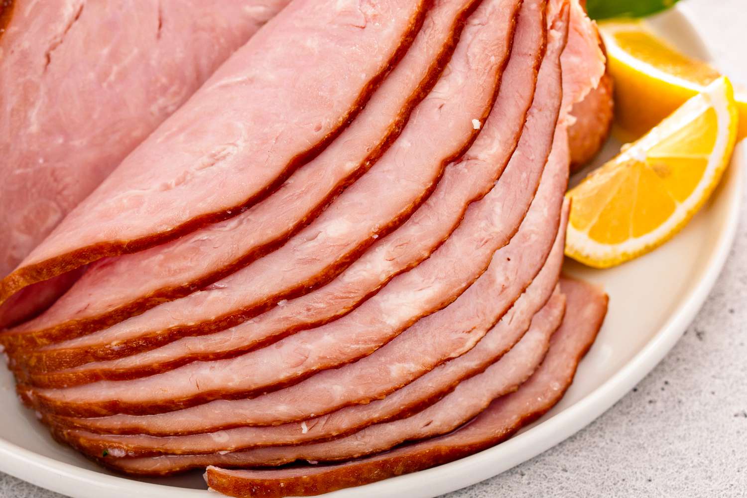 Spiral sliced ham on a platter with orange slices all on a gray countertop