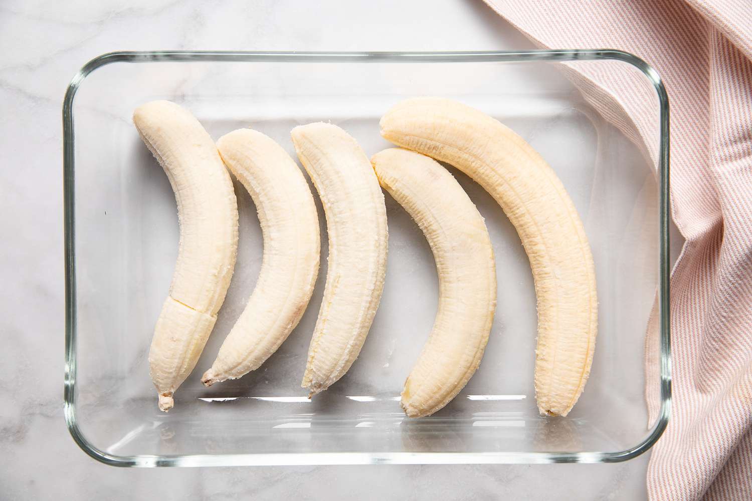 Peeled Bananas in a Glass Baking Dish Next to a Blush Pink Kitchen Towel for Filipino Banana Ketchup Recipe
