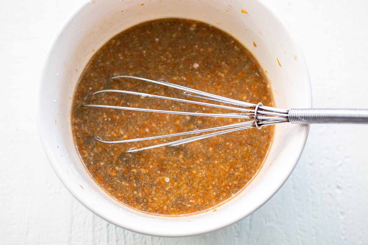 Whisk in a white bowl with ingredients for orange chicken sauce.