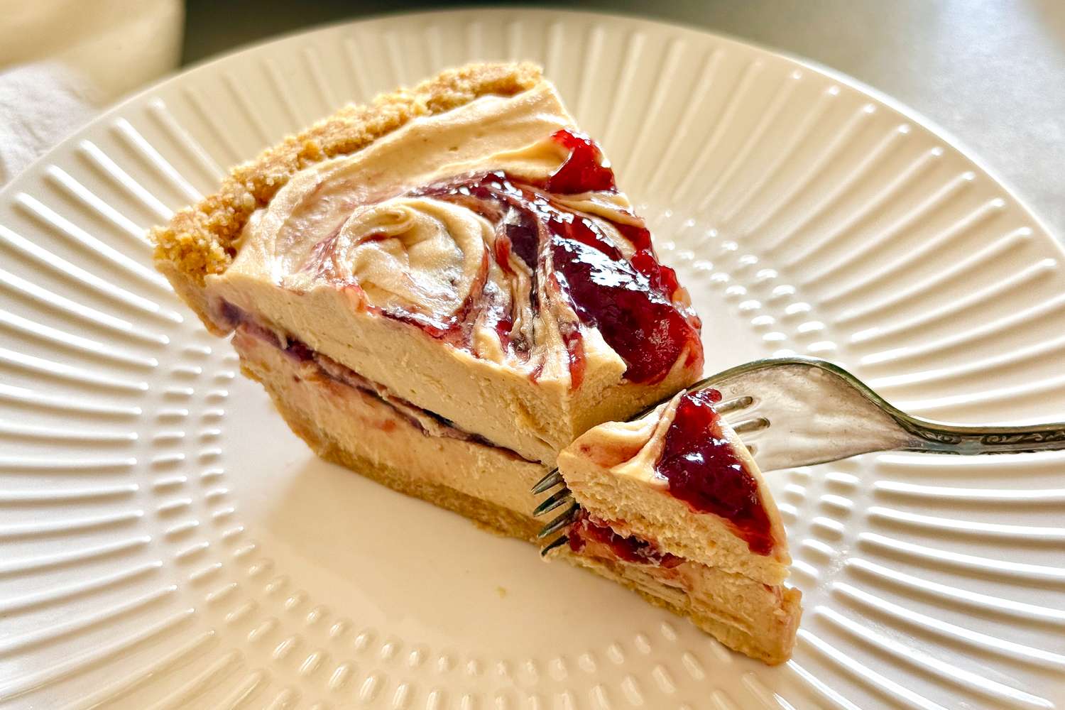 A slice of peanut butter pie with a fork removing a piece featuring swirls of jelly on a plate