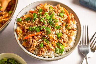 Angled view of a bowl of egg roll in a bowl next to two forks and bowl of sliced green onions