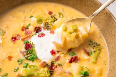 A spoonful of broccoli potato soup garnished with scallions bacon and cream