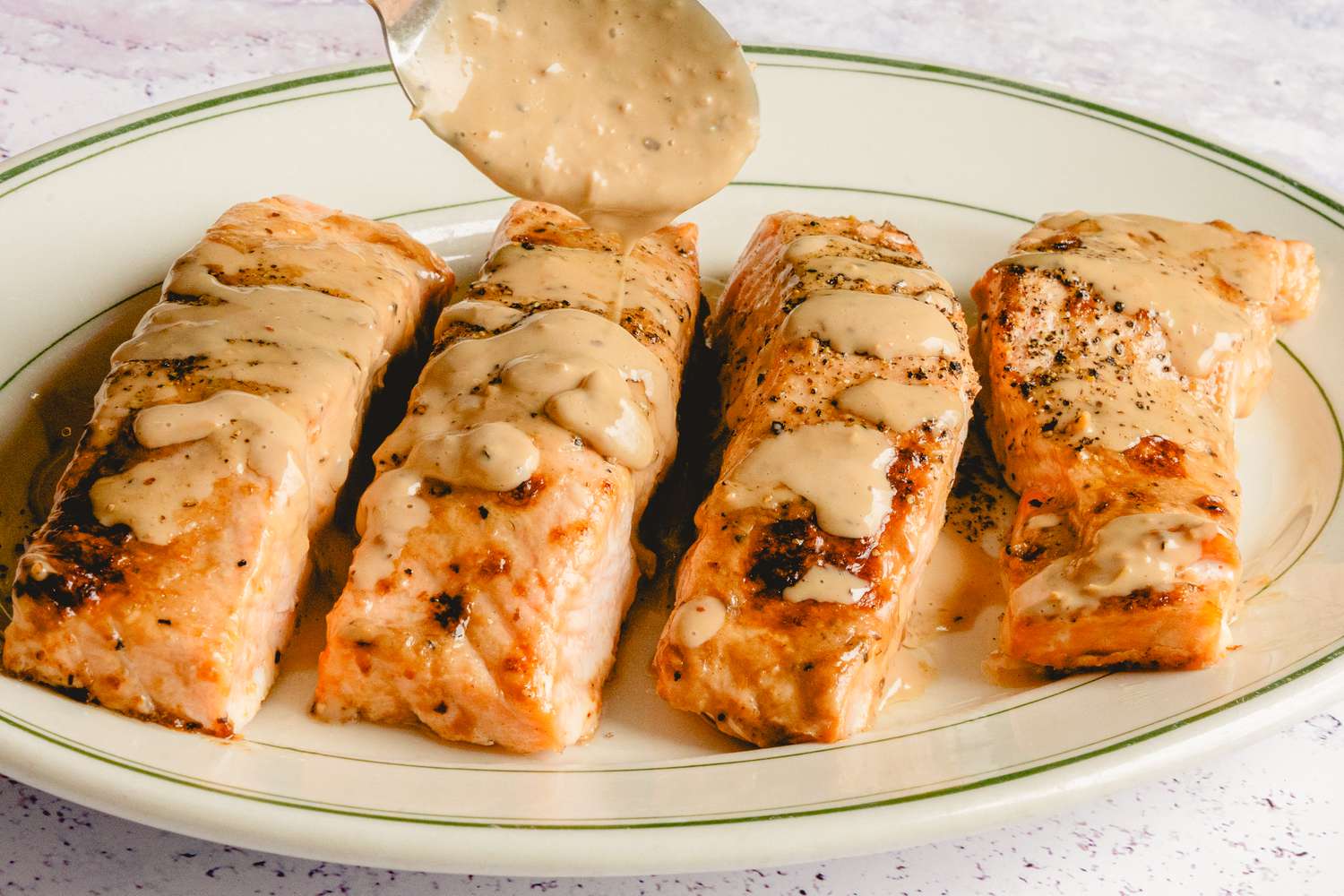 Salmon fillets on a plate with sauce being poured over them