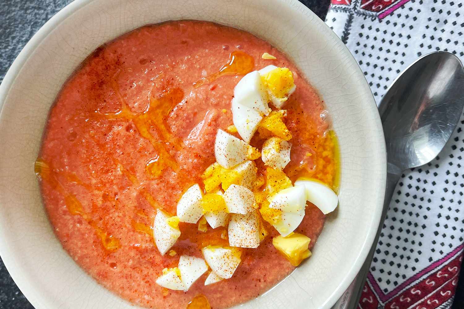 A bowl of creamy tomato soup with chopped boiled eggs on top, spoon and napkin beside