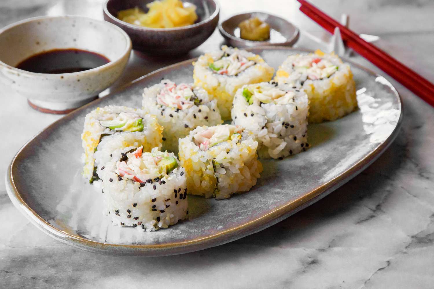 California Rolls on a Plate Next to a Small Bowl of Soy Sauce, Small Bowl of Pickled Ginger, and Small Saucer of Wasabi