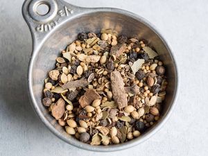 Pickling spice in a measuring cup: cinnamon, bay leaves, yellow mustard seeds, coriander seeds, black peppercorns, dill seeds, alspice berries, red pepper flakes