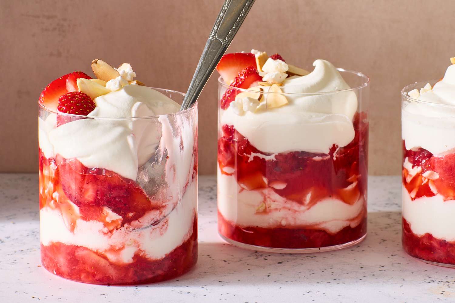 Glasses of a layered strawberry and cream dessert called Eton Mess, garnished with sliced almonds and strawberries