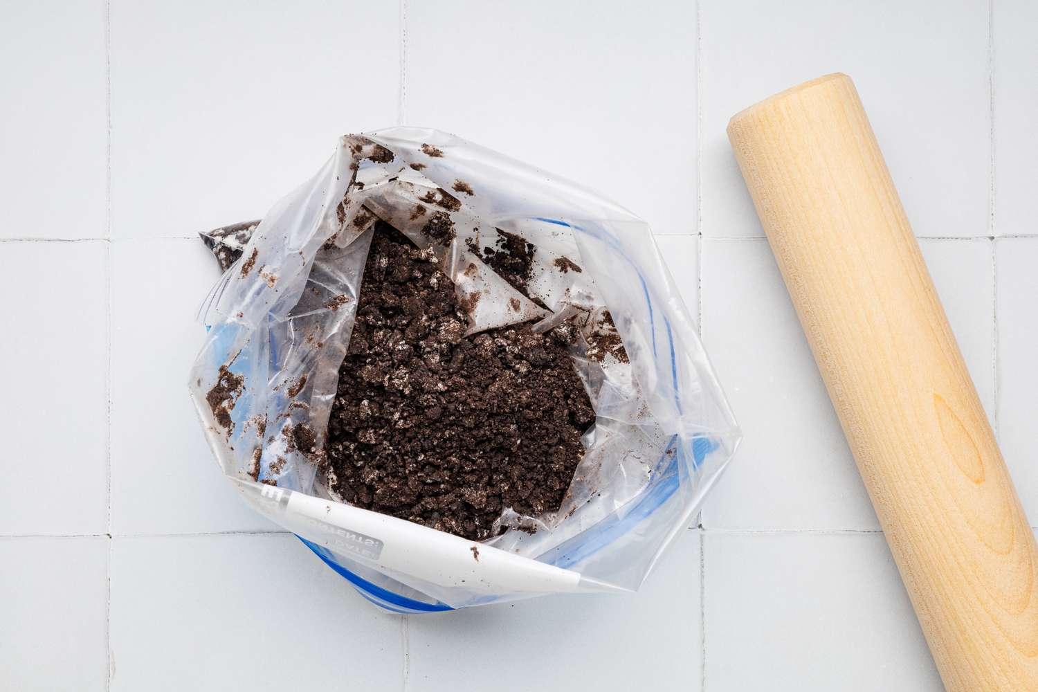 Making the Crunchies: Crushed Cookies in a Plastic Baggy Next to a Rolling Pin for Cookies & Cream Ice Cream Cake Recipe