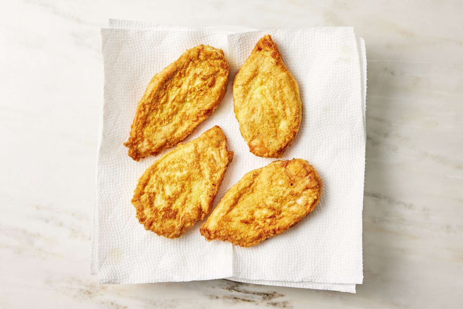 pan fried chicken drying on a plate of paper towels for Chicken Francese recipe