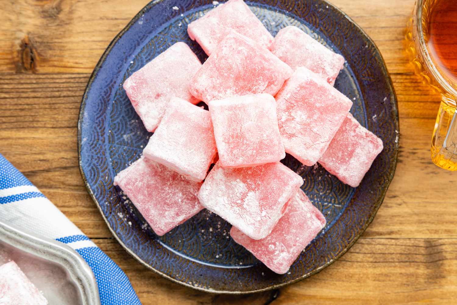 Turkish Delight on a Plate on a Wooden Counter Next to a Cup of Tea and a Kitchen Towel