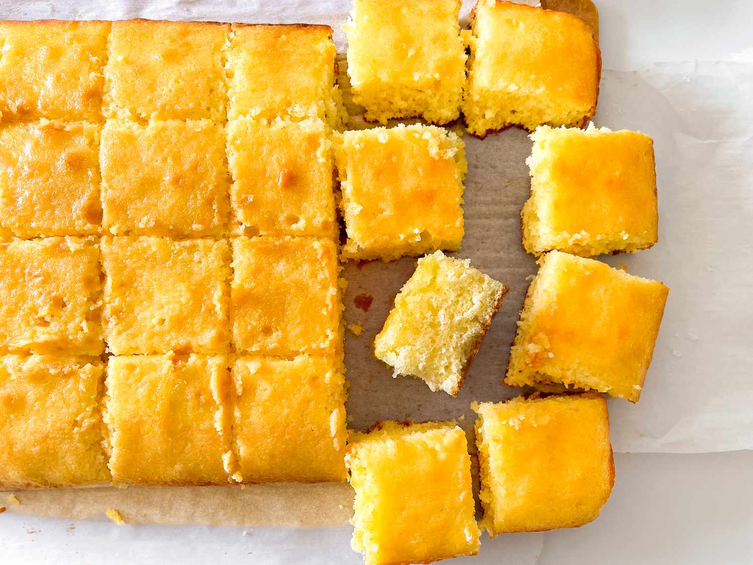 A tray of evenly cut yellow sponge cake squares some pieces are removed and rearranged - Mary Berry’s Lemon Drizzle Traybake Cake